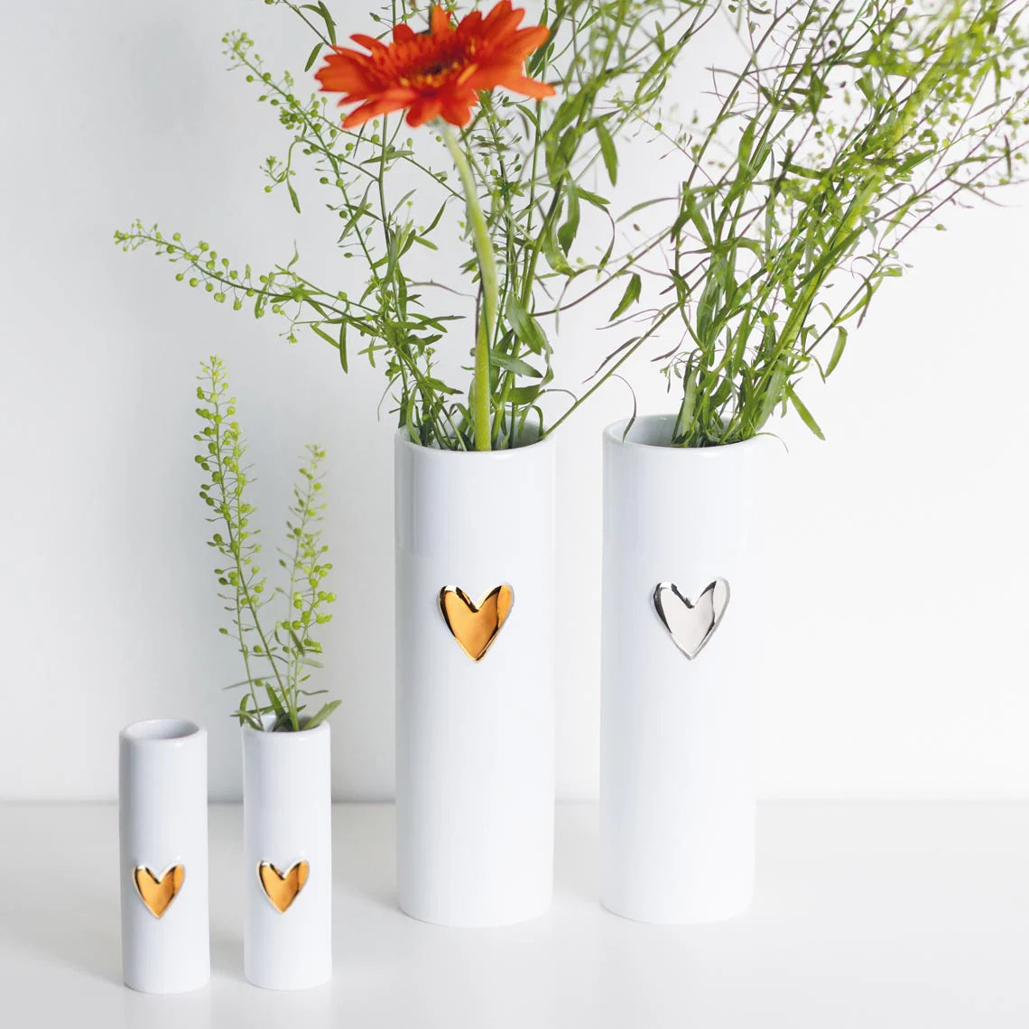 Three white vases with heart designs containing plants on a light background