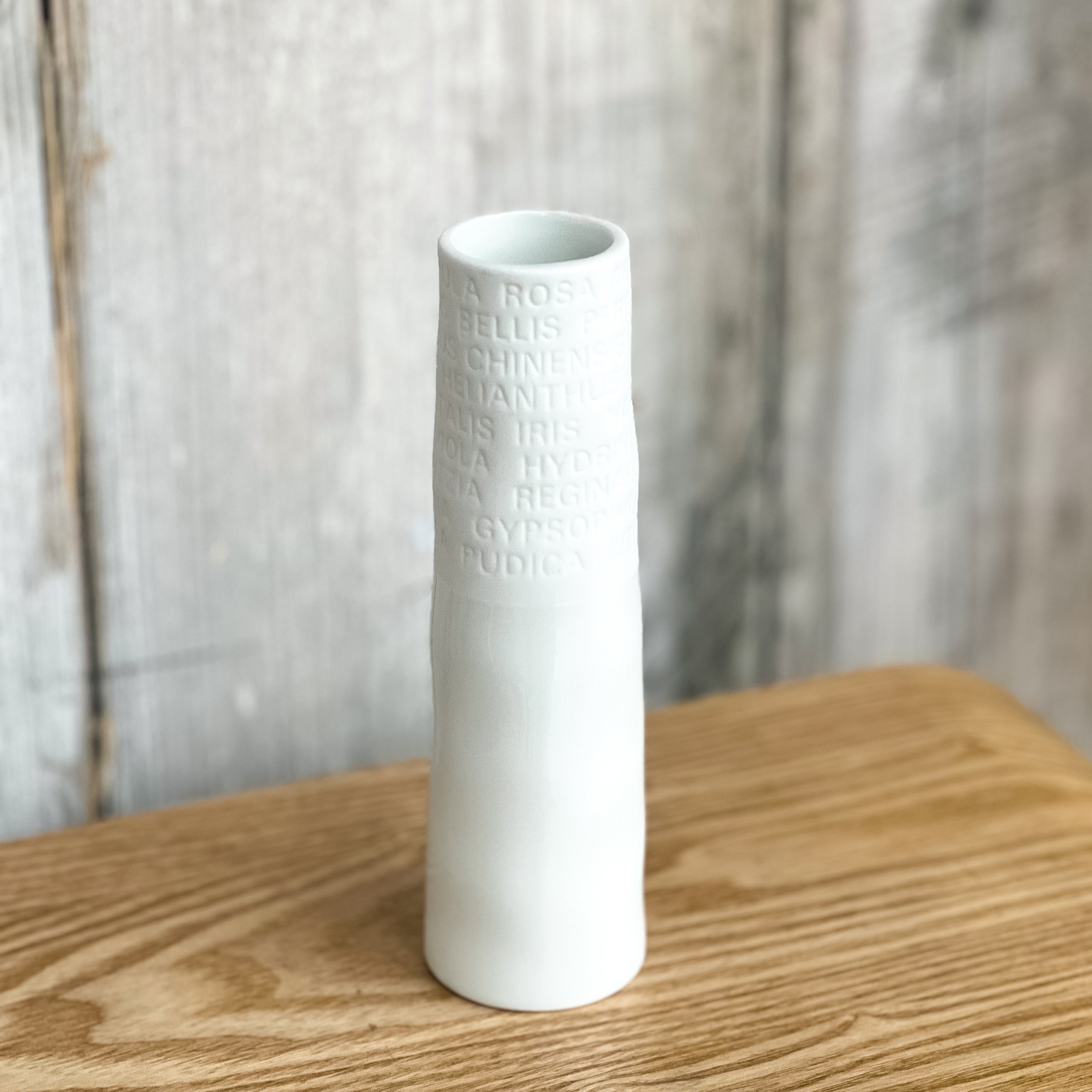 White textured vase on a wooden surface with a blurred natural background