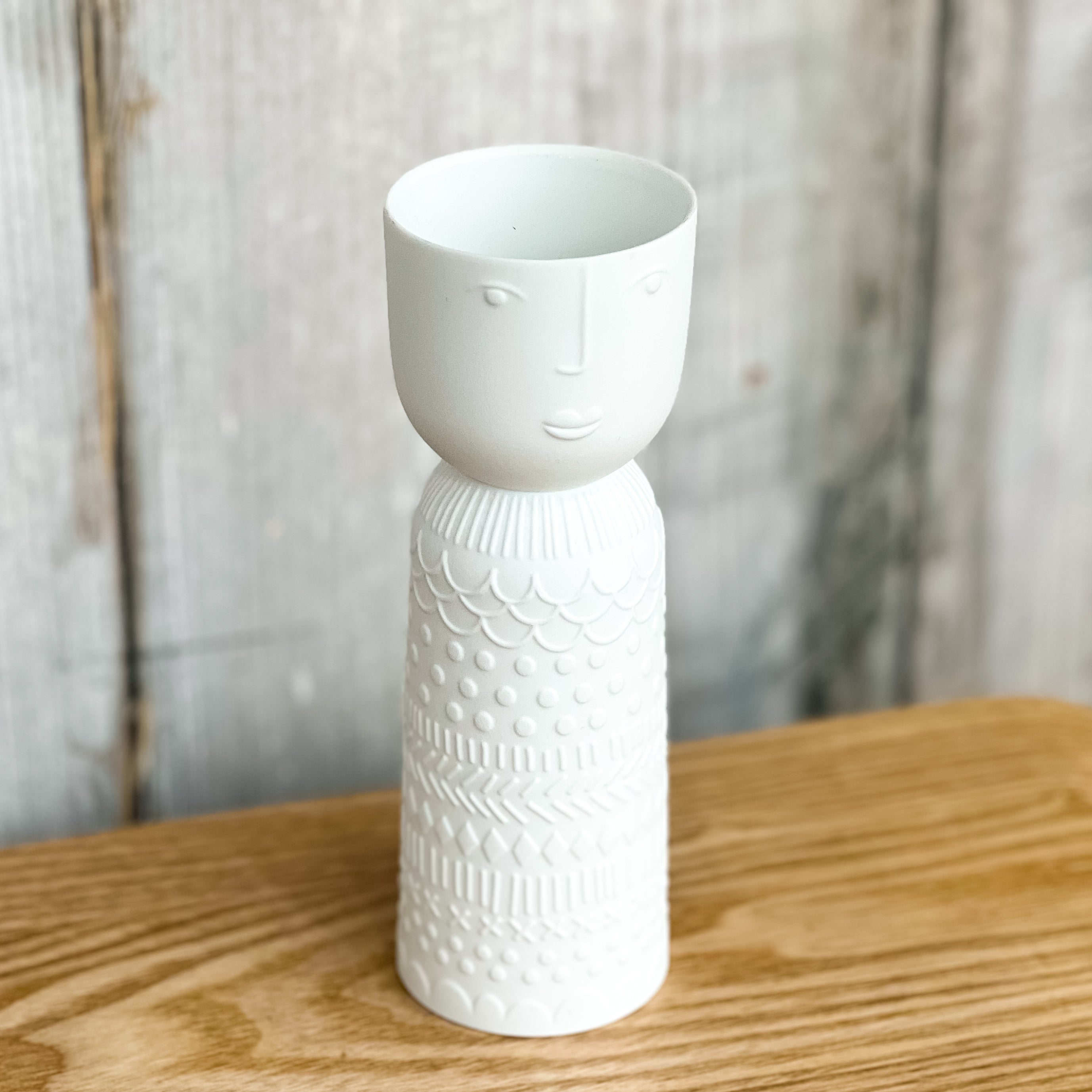 White ceramic vase with face design on a wooden surface