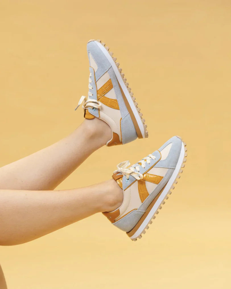 A pair of mustard yellow and blue sneakers on legs in the air