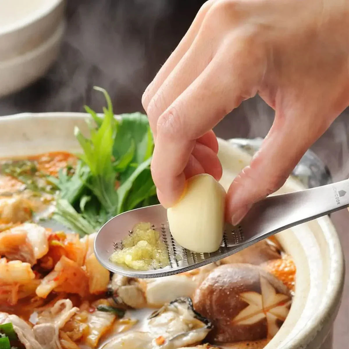 A person grating garlic on a spoon over a cooking pan
