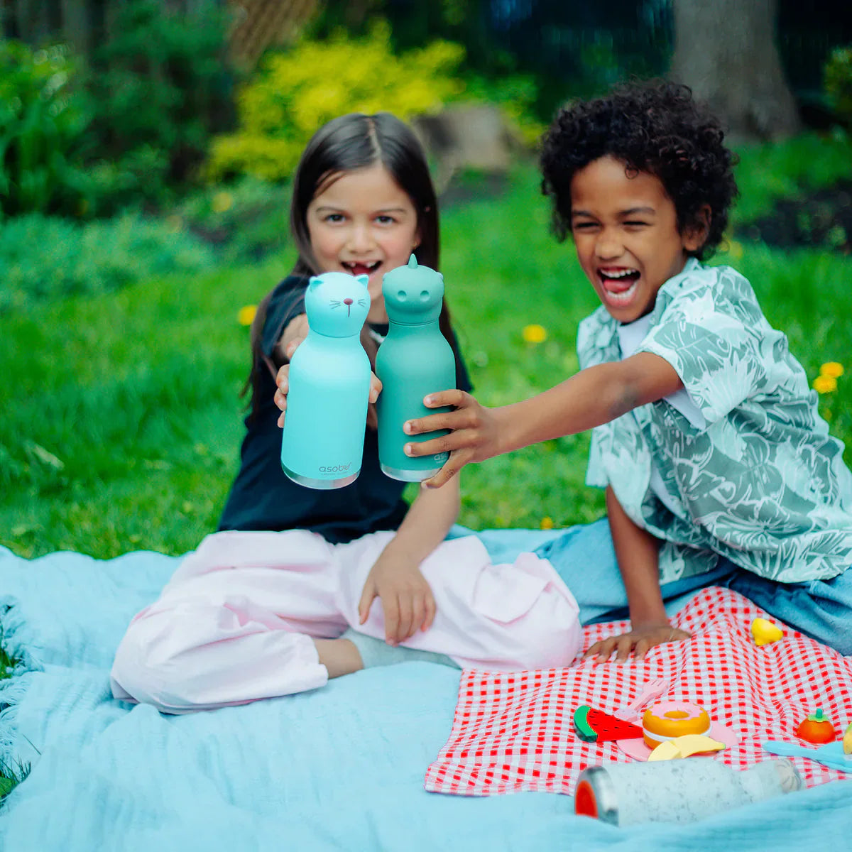 Two children on a picnic blanket holding blue water bottles