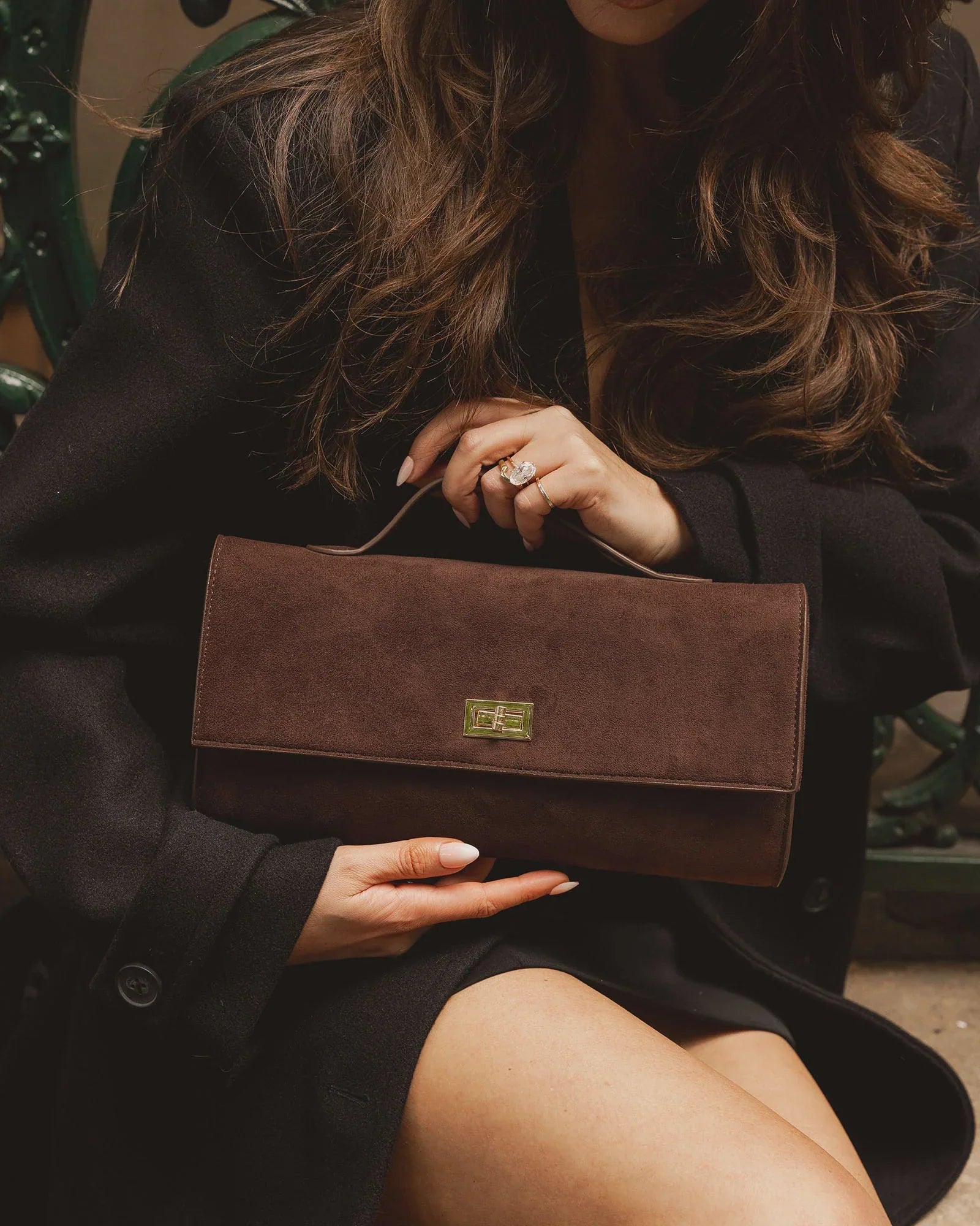 A woman holding a chocolate brown clutch handbag