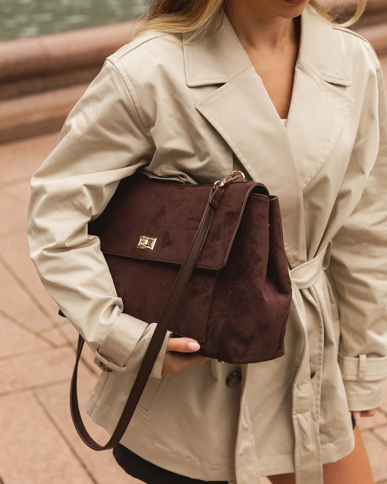 A woman wearing a cream coat carrying a brown handbag under her arm