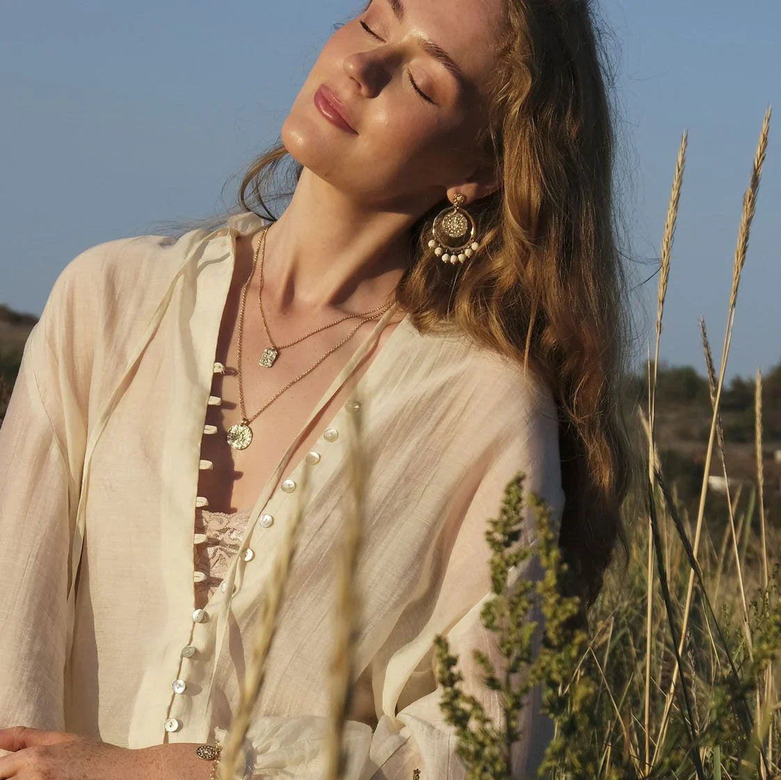 A woman sitting in the grass in sunshine wearing jewellery 