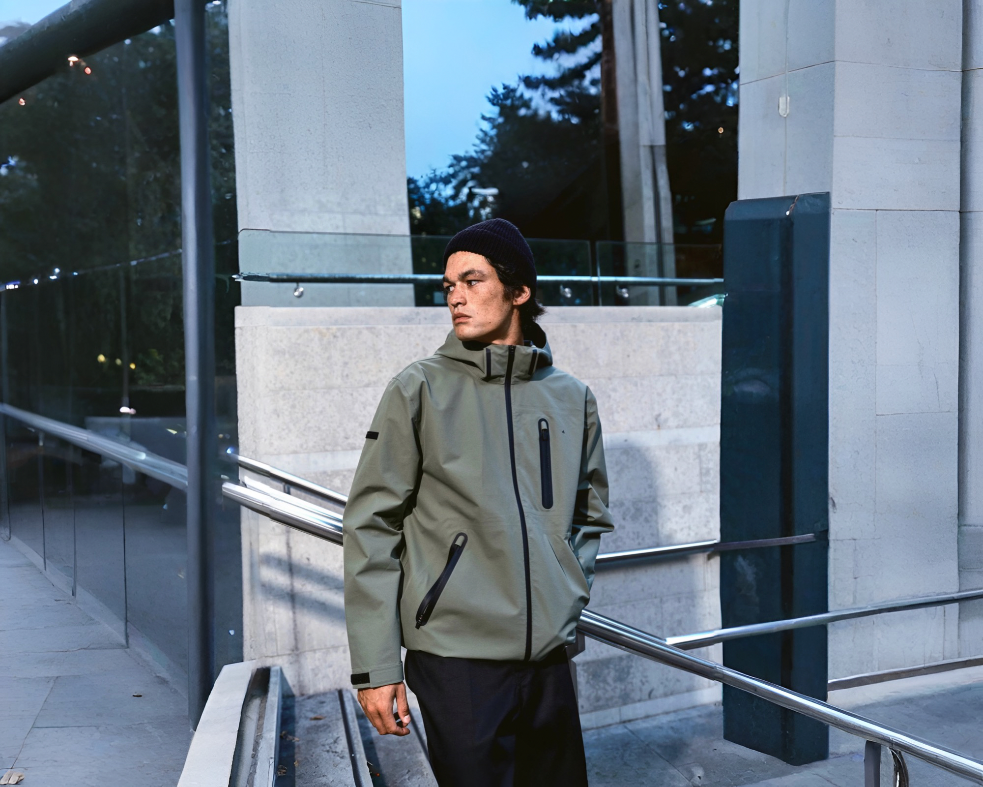 Man walking down stairs wearing a green raincoat and a beanie