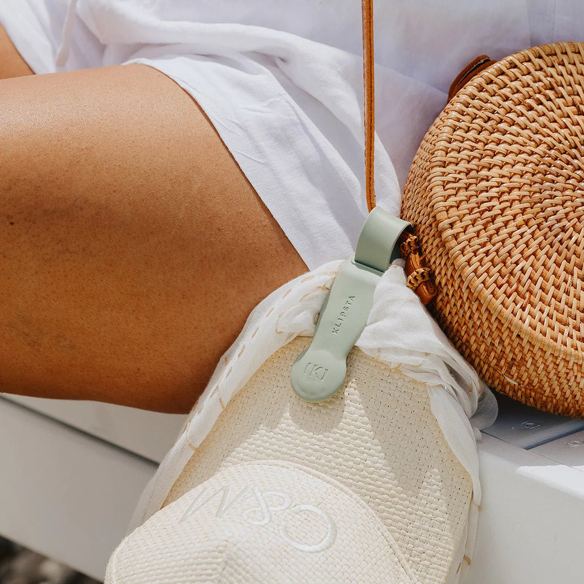 A green clip holding a cream cap onto a rattan handbag