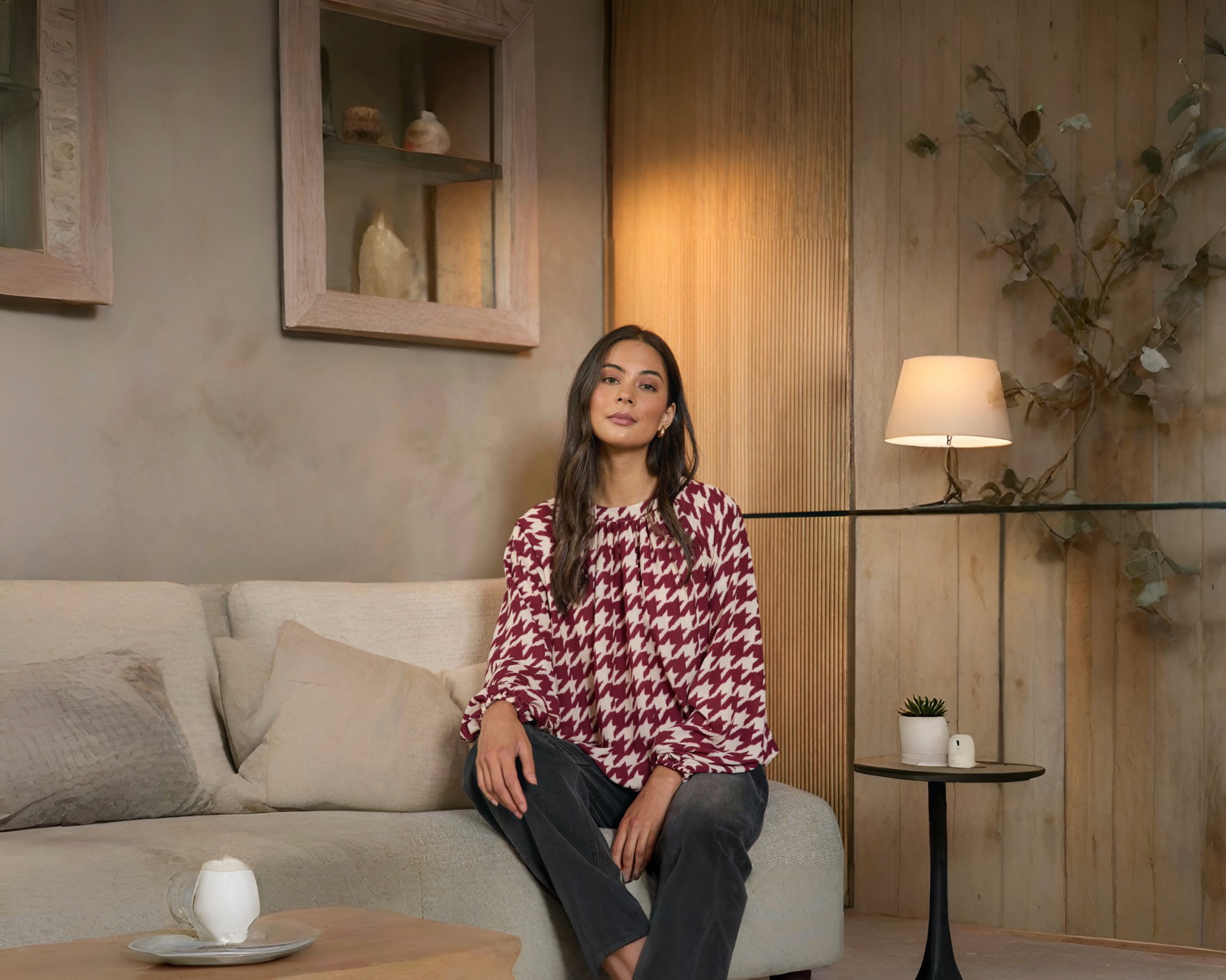A woman sitting on a couch wearing a red and cream houndstooth blouse