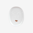 White ceramic face-shaped plate with a stylized face design on a white background
