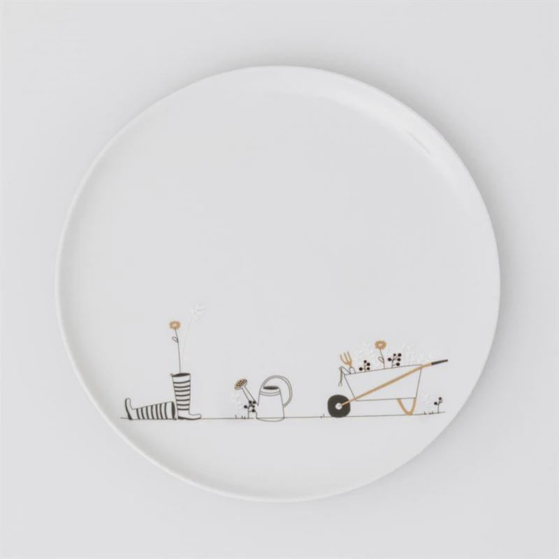 White plate with black and gold illustrations of a wheelbarrow, watering can, and boots on a white background