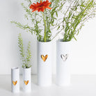 Three white vases with heart designs containing plants on a light background