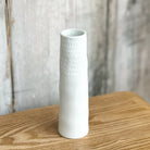 White textured vase on a wooden surface with a blurred natural background