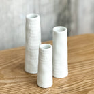Three white textured vases on a wooden surface with a blurred background
