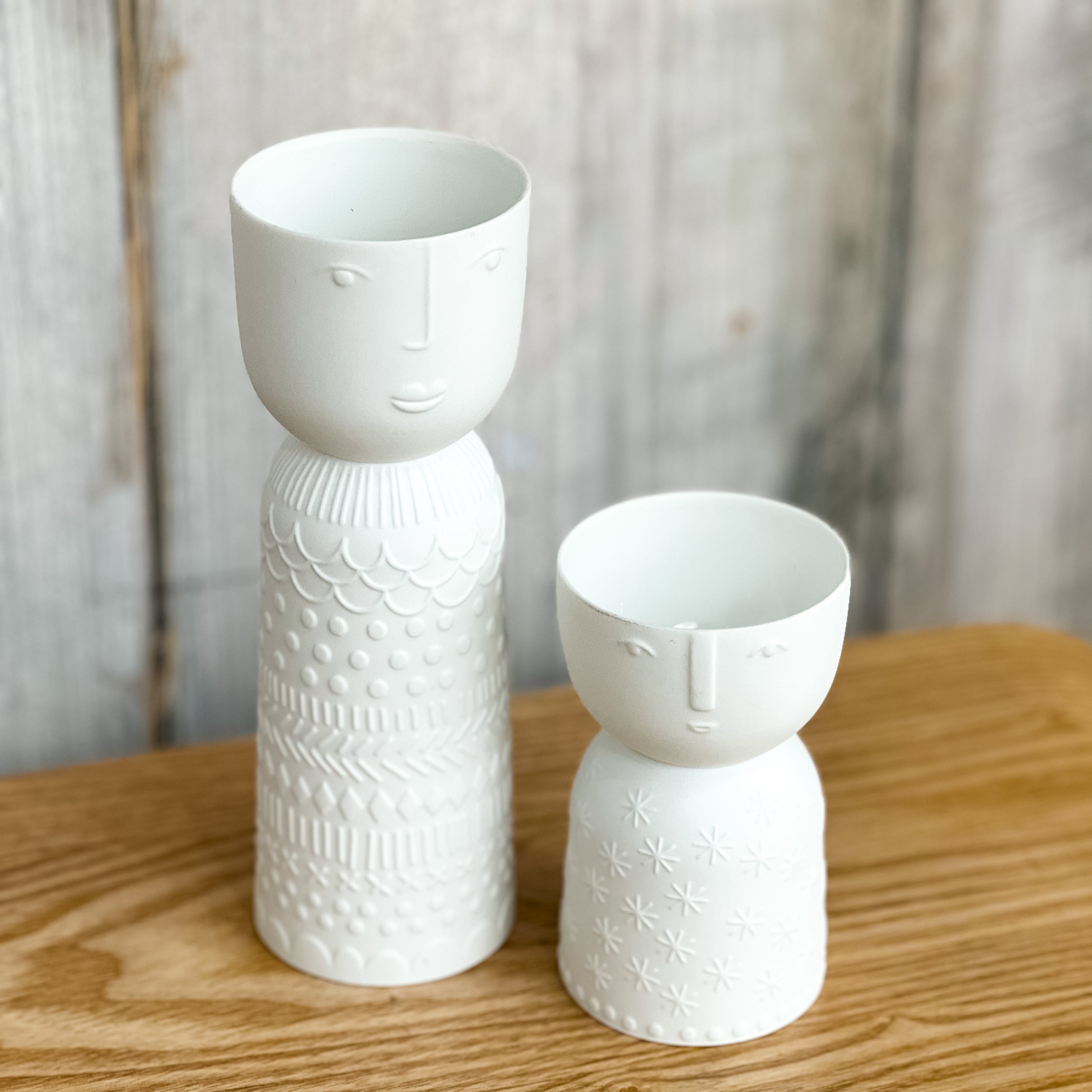 Two white ceramic vases with face designs on a wooden surface.