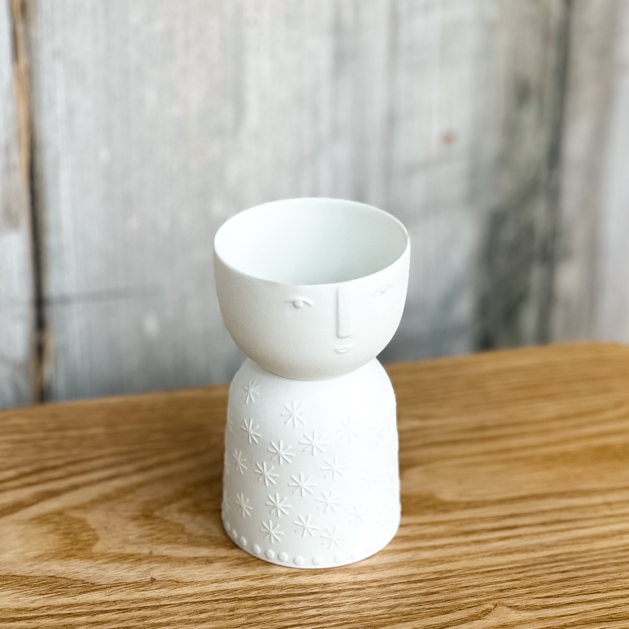 White ceramic vase with floral patterns and a face on a wooden surface